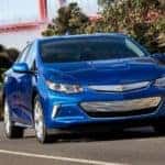 Blue 2016 Chevrolet Volt sedan driving down a paved road in front of an orange bridge