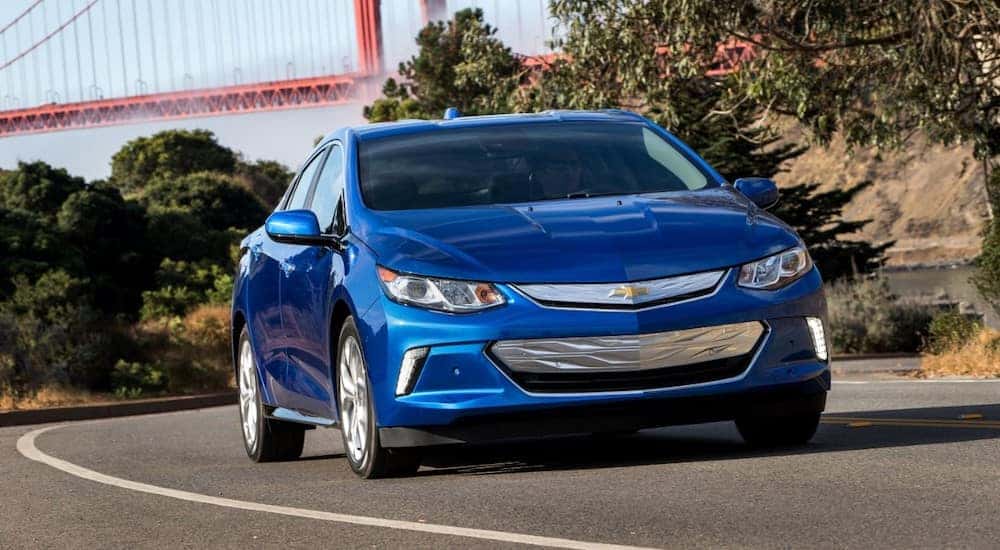 Blue 2016 Chevrolet Volt sedan driving down a paved road in front of an orange bridge