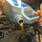 Hands holding a container of fresh oil and pouring it under the open hood of a vehicle