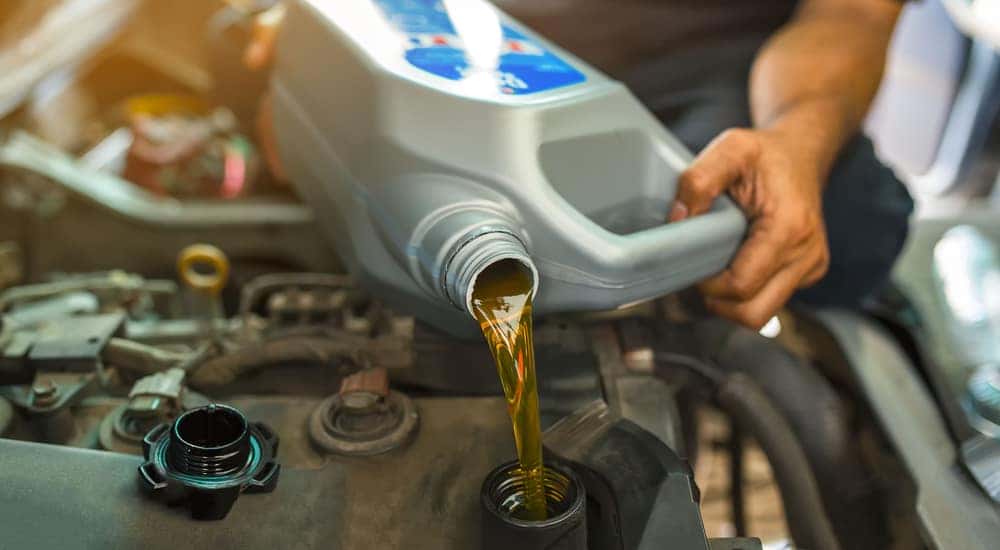 Hands holding a container of fresh oil and pouring it under the open hood of a vehicle