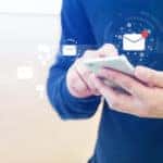 Man in a blue sweat holding a smartphone with notification symbols floating out of it