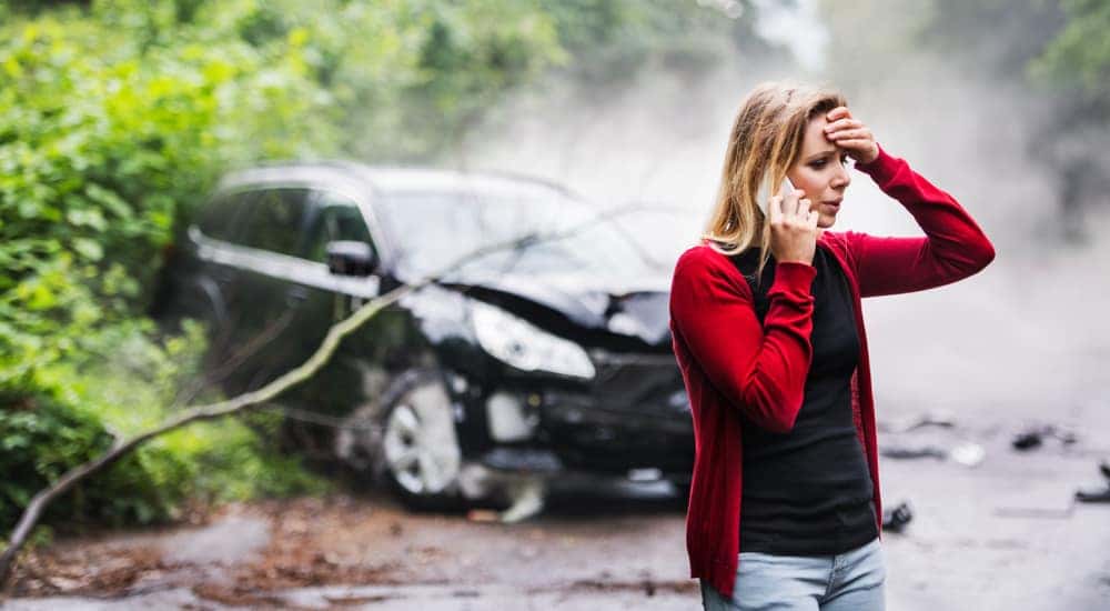 Woman in a red cardigan distressed on the phone in front of her smashed up vehicle
