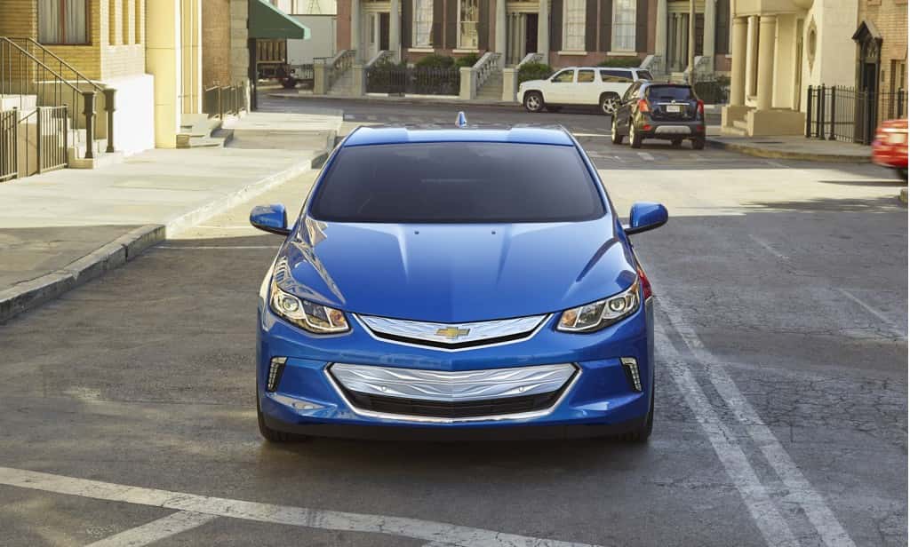 Front view of a blue 2016 Chevy Volt sedan driving through a city neighborhood