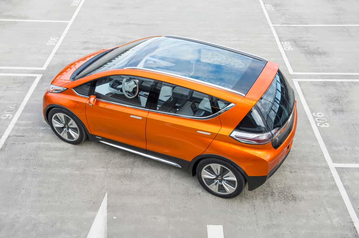An orange 2015 Chevy Bolt EV concept is shown parked in an empty lot from above.