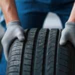 Man in blue pants and grey gloves holding a tire upright