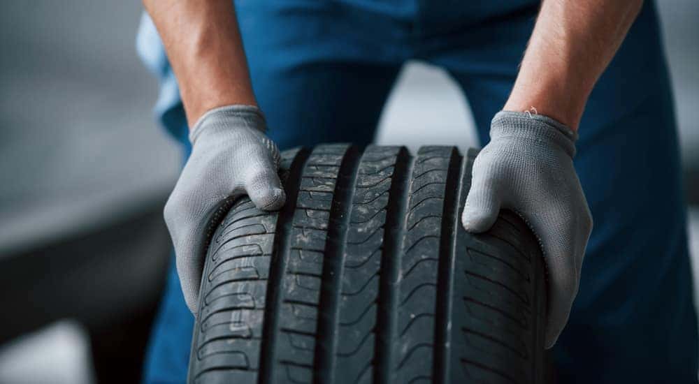 Man in blue pants and grey gloves holding a tire upright