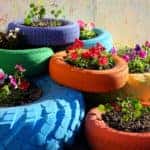 Tires of various sizes painted blue, green, orange, red, purple, and yellow and stacked on top of one another with plants in the center