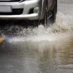 Tires of a silver vehicle driving down a flooded, paved road