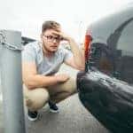 Man in khakis looking at the large scratches on his vehicle