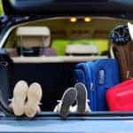 Two sets of feet poking out next to luggage in the open trunk of a blue vehicle