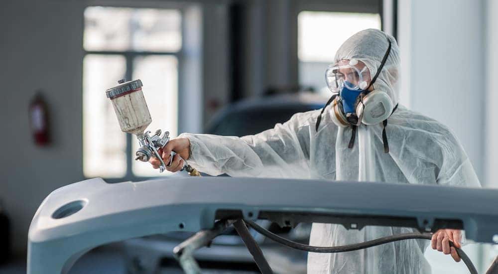 Mechanic in a white paint suit and mask using a paint sprayer on a vehicle