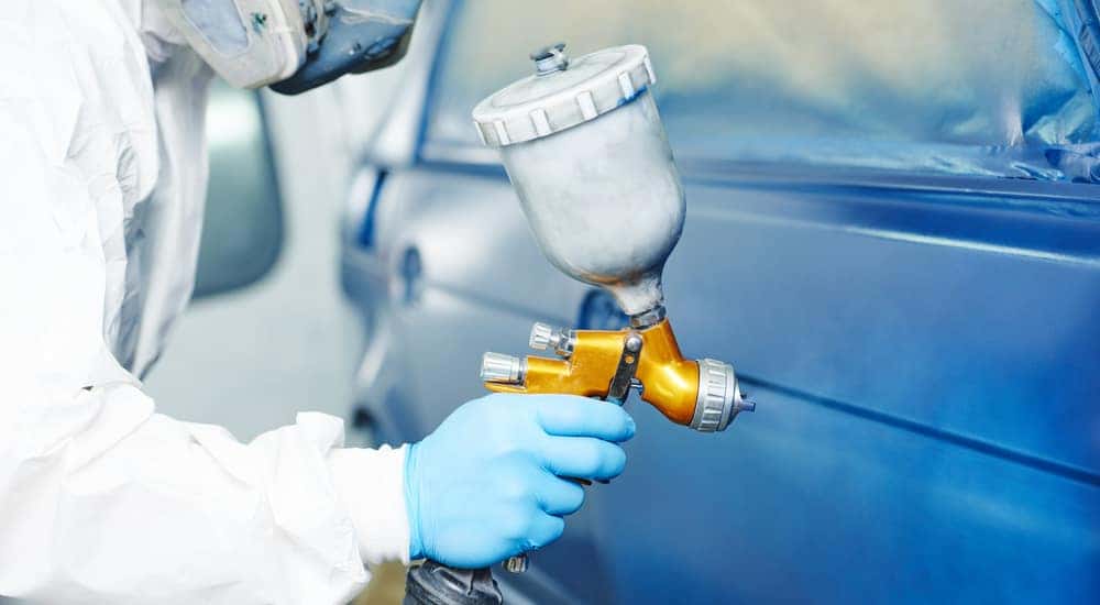 Person in a white suit and mask painting a blue vehicle with a professional paint tool