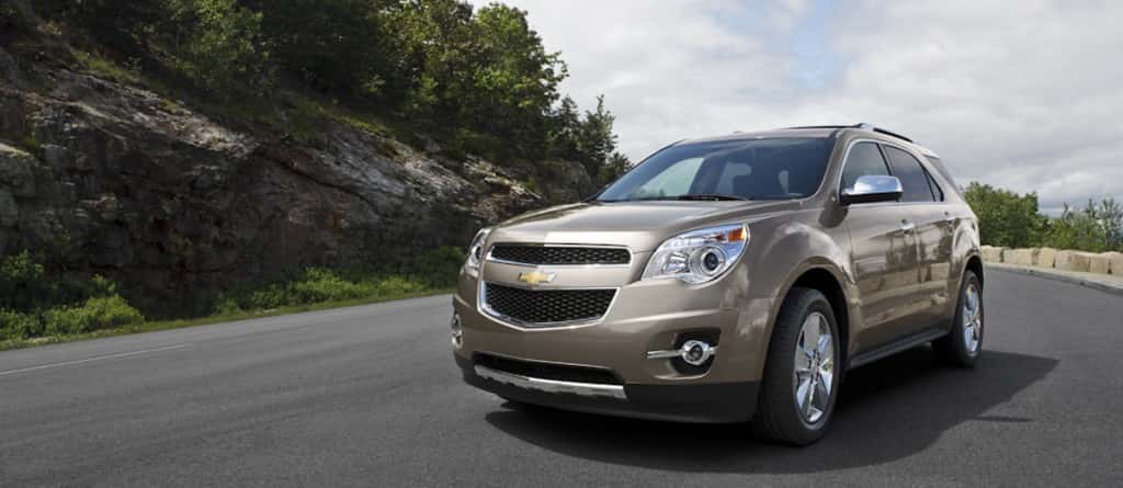 Front view of a tan Chevy Equinox for sale driving down a winding road