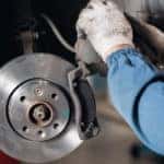Mechanic in a blue shirt and white gloves working on the brakes of a vehicle