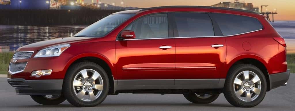 Side view of a red Chevy Traverse for sale parked by a pier at dusk