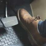 Foot in a brown leather shoe pressing on the gas pedal in a vehicle, next to the brakes