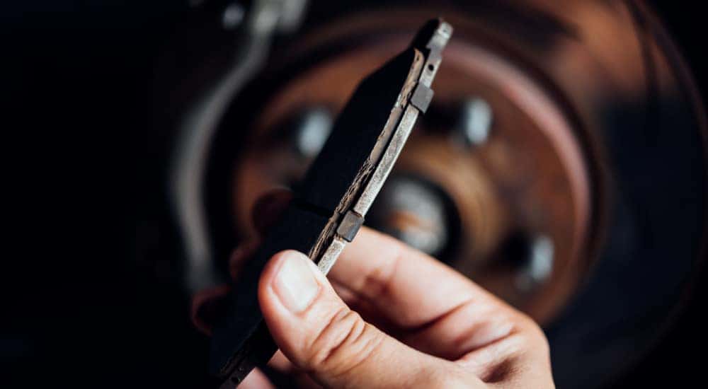 Hand holding a brake pad in front of a wheel