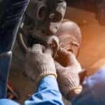 Mechanic in a blue jumpsuit and grey gloves performing repairs on vehicle brakes