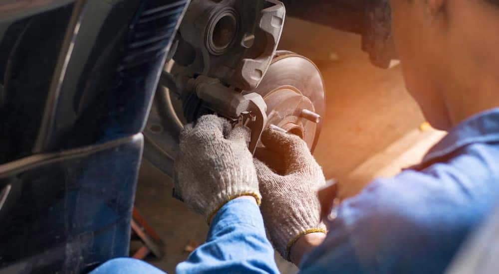 Mechanic in a blue jumpsuit and grey gloves performing repairs on vehicle brakes