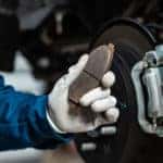 Mechanic wearing a blue shirt and white gloves holding a brake pad