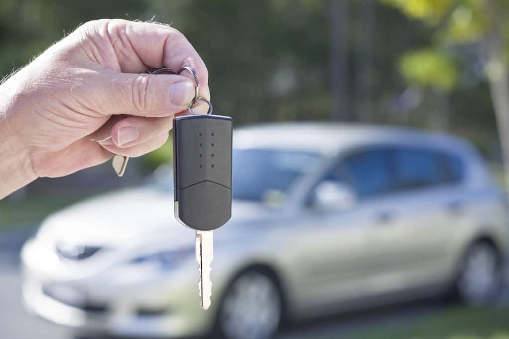 Hand holding up a key in front of a silver vehicle