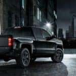 Black 2015 Chevrolet Silverado truck parked in a dark alley in front of tall city buildings