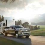 Black 2015 Silverado 3500HD truck pulling a camper past tall mountains and flat green land