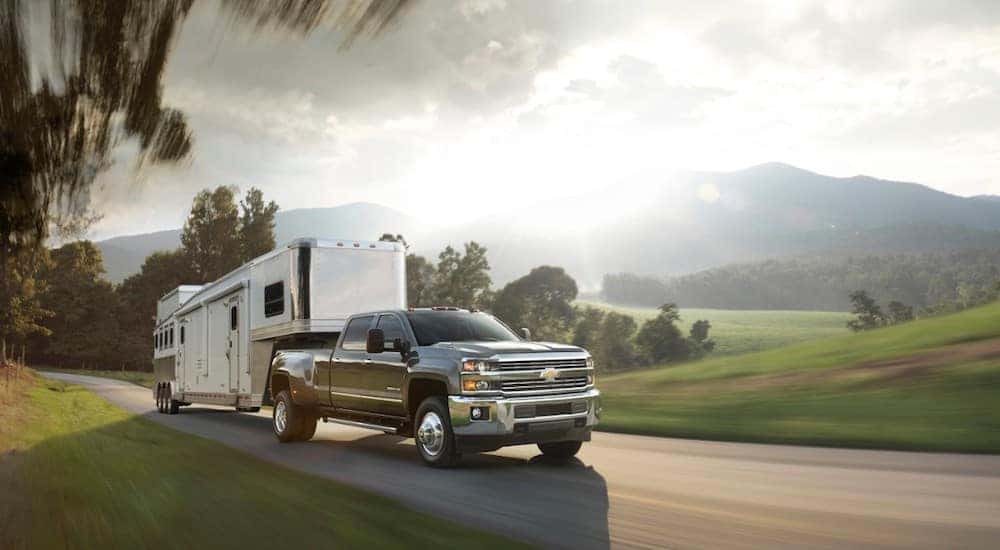 Black 2015 Silverado 3500HD truck pulling a camper past tall mountains and flat green land