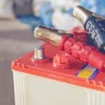 Red and white car battery with black and red plugs on top of it sitting on a cement floor