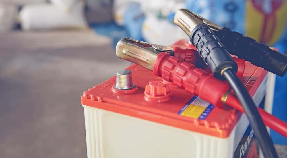 Red and white car battery with black and red plugs on top of it sitting on a cement floor