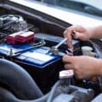 Hands installing and tightening bolts on a new battery under the hood of a vehicle