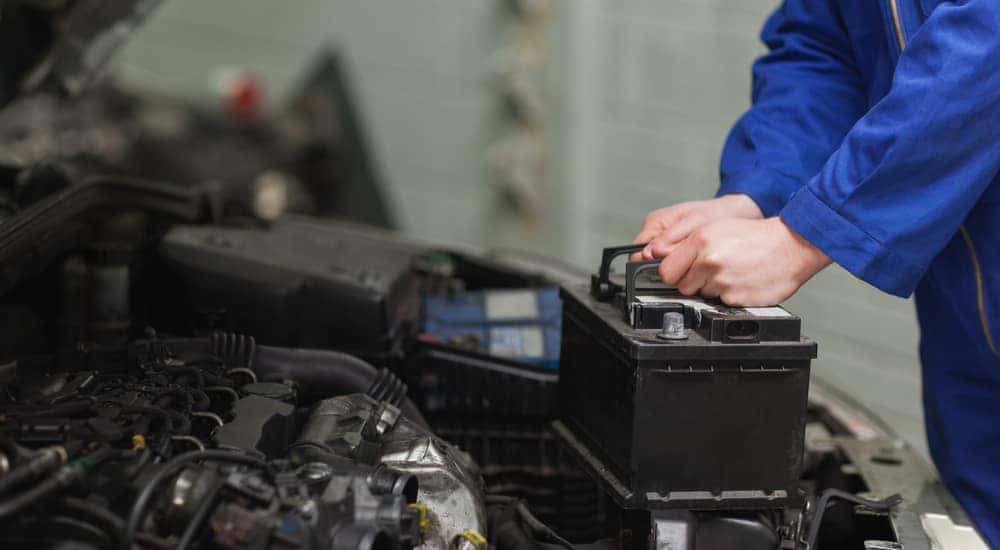 Male mechanic in a blue jumpsuit changing the battery under the hood of a car