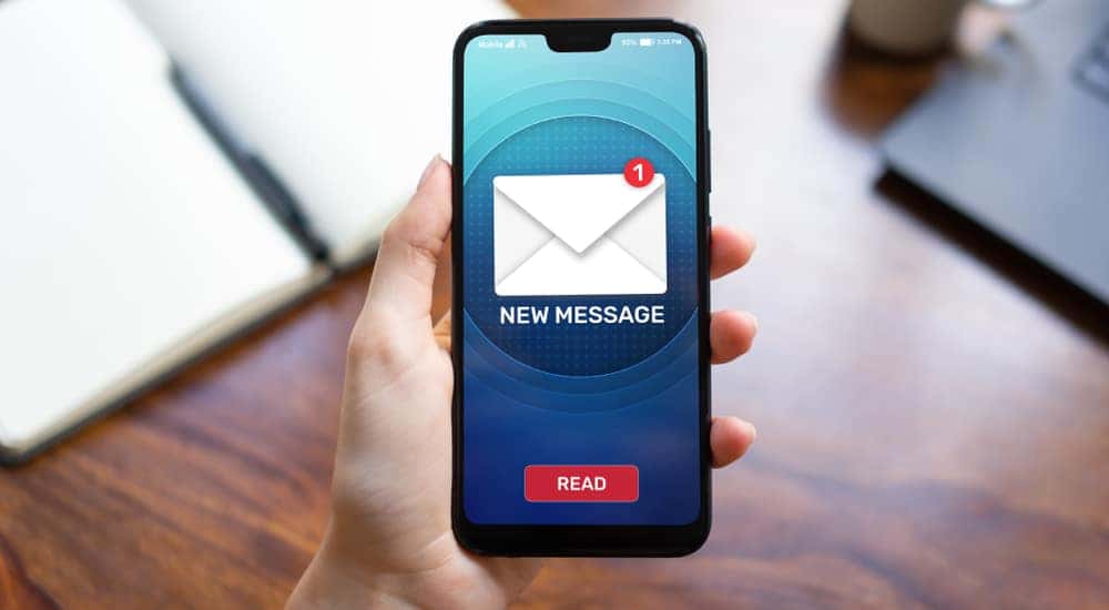 Hand holding a smartphone with an envelope symbol on the screen above a brown desk