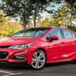 Red 2016 Chevrolet Cruze sedan driving down a paved road past green grass and trees