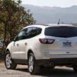 Back to front view of a white 2016 Chevrolet Traverse SUV parked on a dirt ground in front of tall mountains