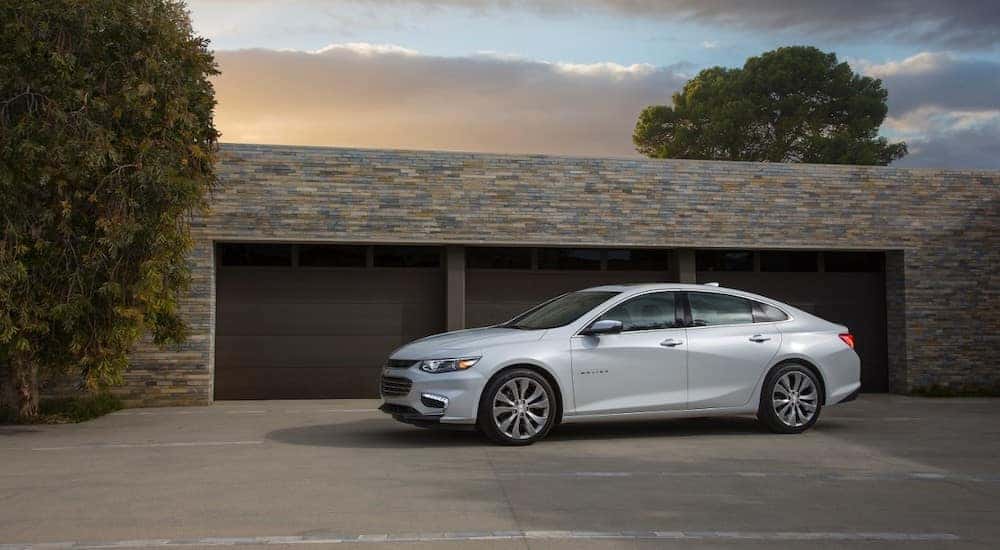 White 2017 Chevrolet Malibu sedan parked in front of three brown garage doors