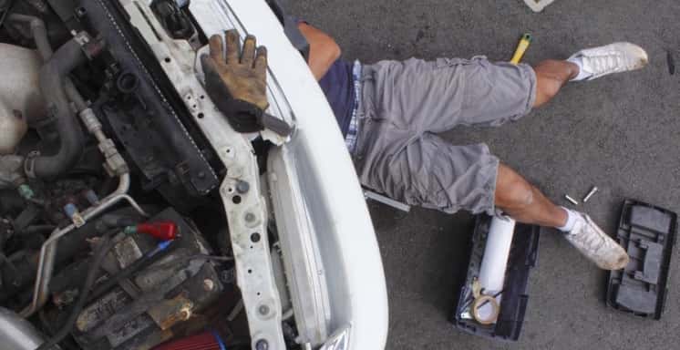 Man in shorts under a vehicle while repairing it