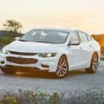White 2016 Chevrolet Malibu parked across a paved road in front of grassy hills
