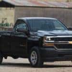Black 2016 Chevrolet Silverado parked in dirt in front of a brown barn
