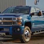 Blue 2016 Chevy Silverado 2500HD pulling a trailer past a large building