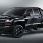 Black 2016 Chevrolet Silverado truck parked on a grey floor, in a spotlight, in front of a grey wall