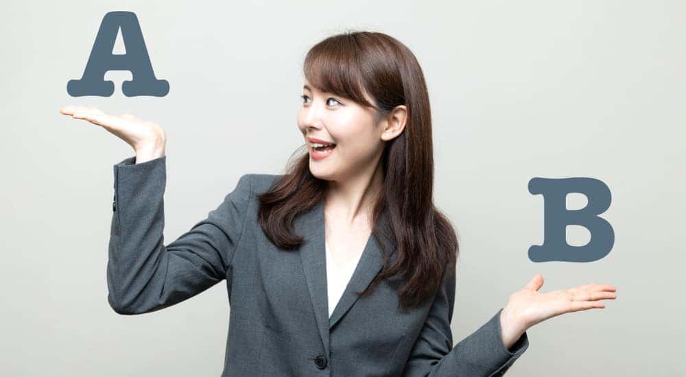 Businesswoman standing her hands out in front of a white wall with one hand below an "A" and one below a "B"