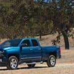 Blue 2016 Chevrolet Silverado pickup truck driving down a dirt path surrounded by grass and trees