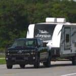 Black Chevrolet Silverado 2500HD truck, with a white camper attached, driving down a paved road