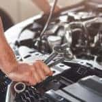 Mechanic leaning over the open hood of a vehicle with wrenches in hand