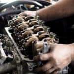 Man's hands working on a car's engine with the cover off of it