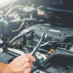 Vehicle mechanic holding a wrench over the open hood of a vehicle and examining the engine