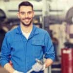Mechanic in a blue jumpsuit holding a wrench in front of a lifted minivan in a garage