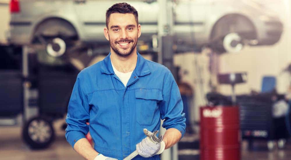 Mechanic in a blue jumpsuit holding a wrench in front of a lifted minivan in a garage