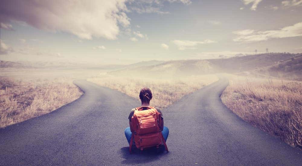 Woman wearing an orange backpack sitting at the corner of a crossroads